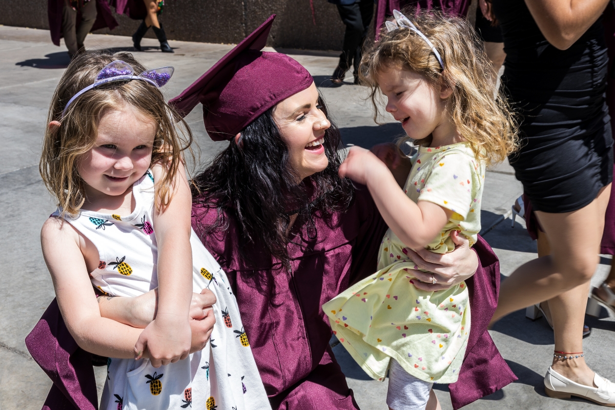 Woman in maroon cap and gown holds two young daughters