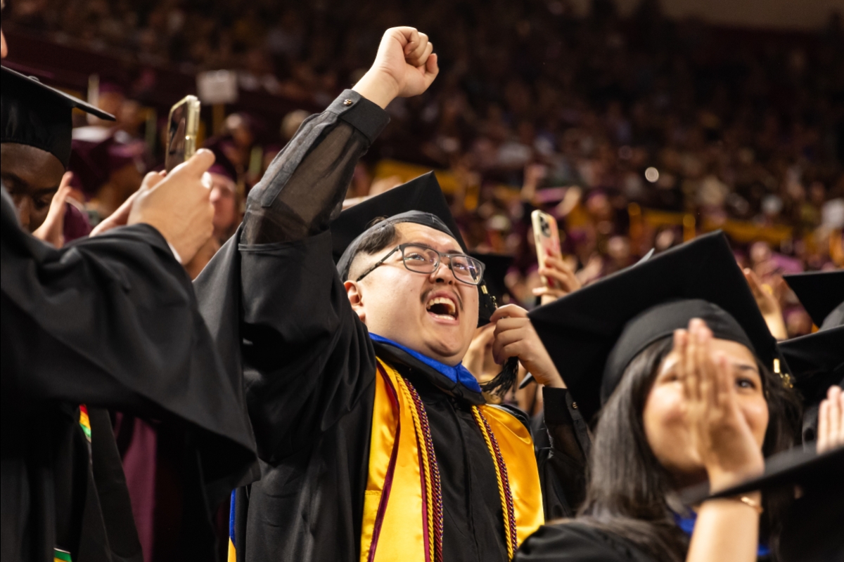 Student in black graduation robe raising fist in air and cheering