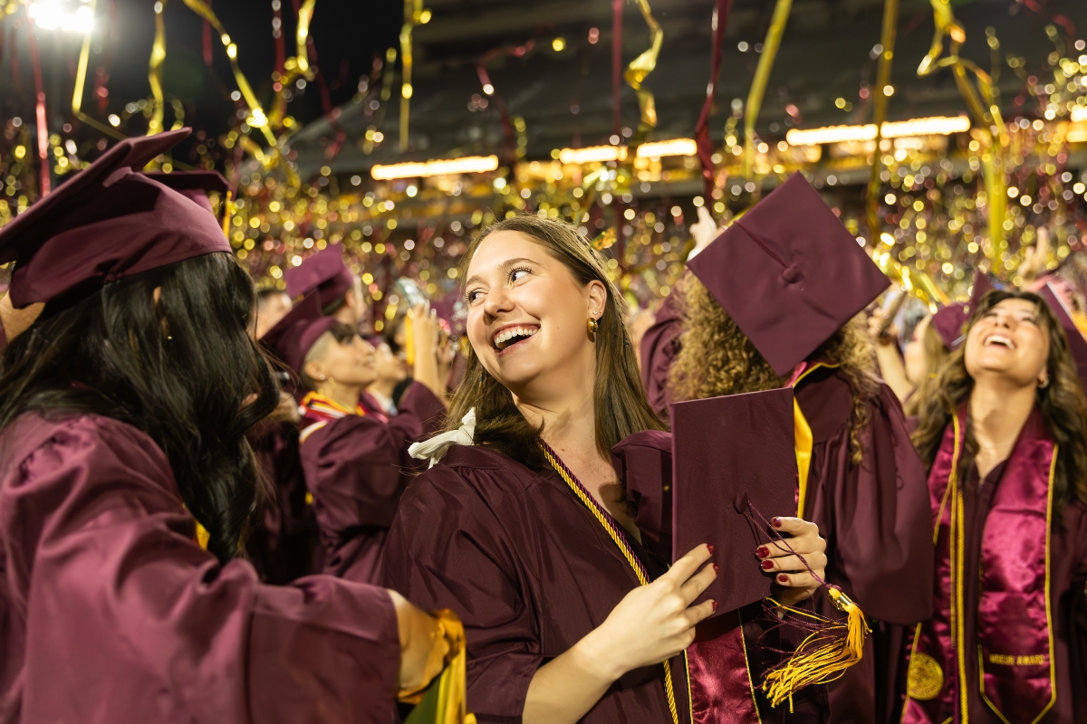 Graduates smiling as streamers fall overhead during commencement