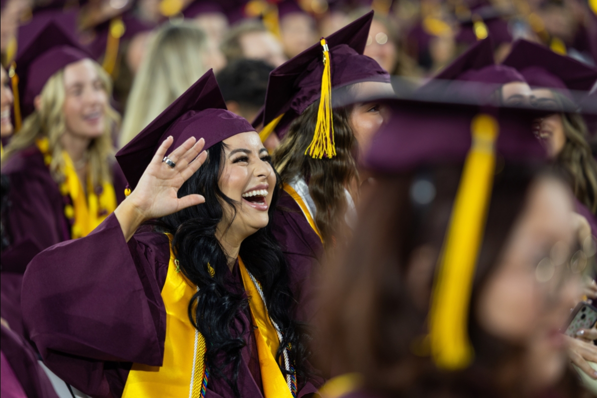 ASU graduate in cap and gown smiles and waves from crowd during convocation