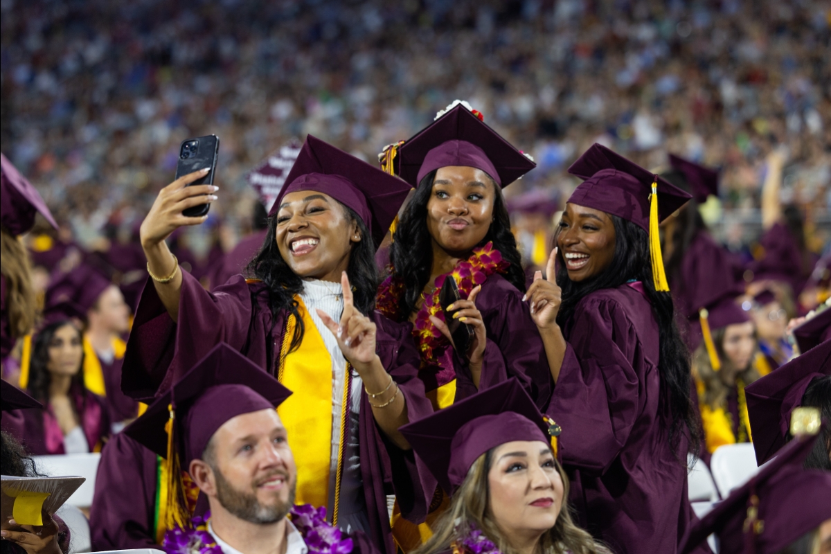 Three ASU graduates on field take a selfie