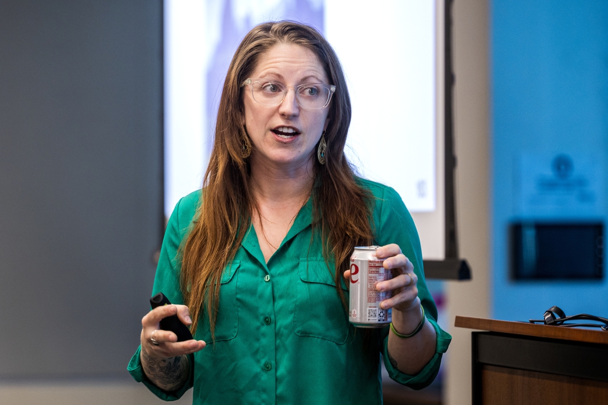 Woman with long hair and green blouse holding soda can giving presentation