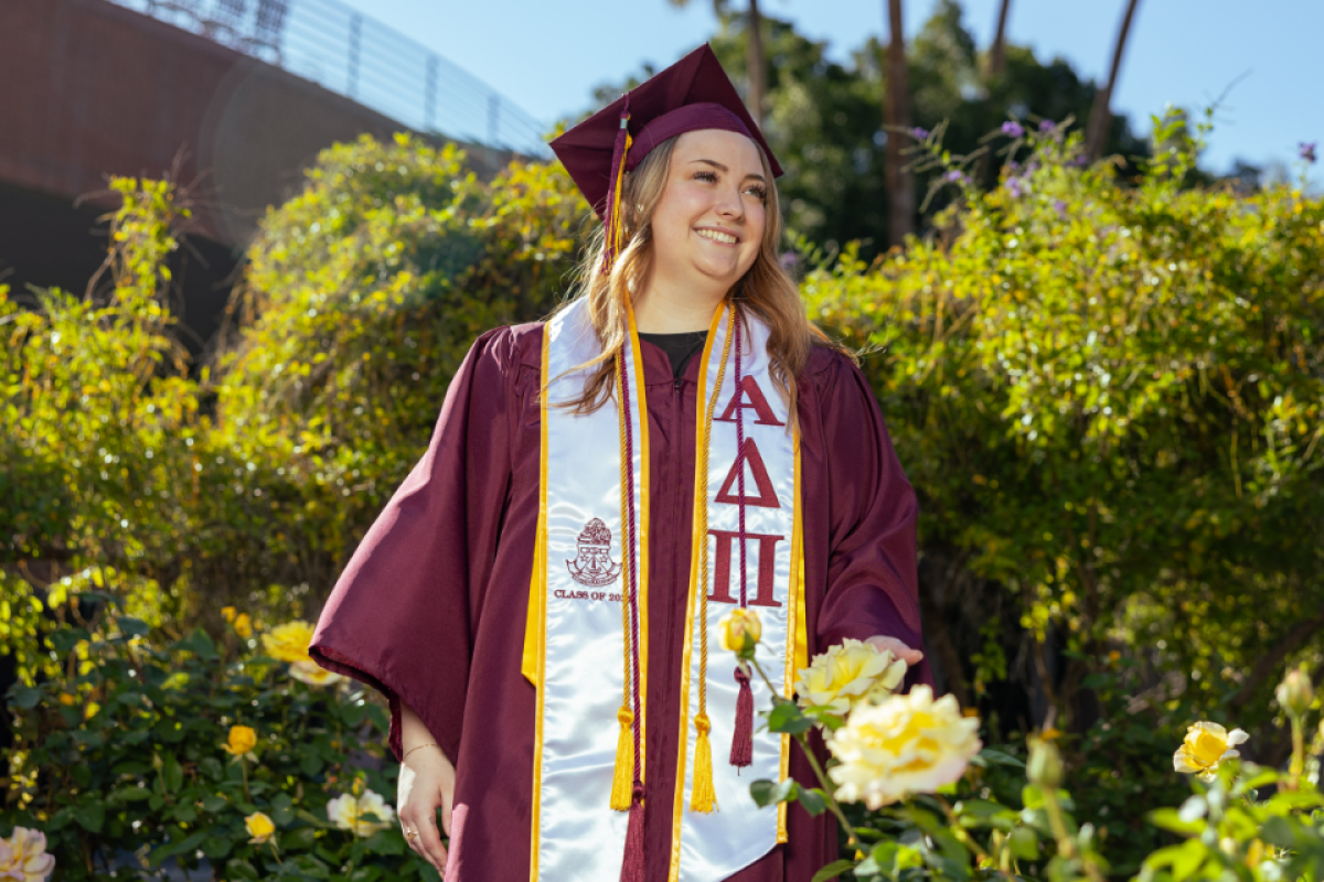 An ASU graduate in commencement regalia looks into the distance smiling