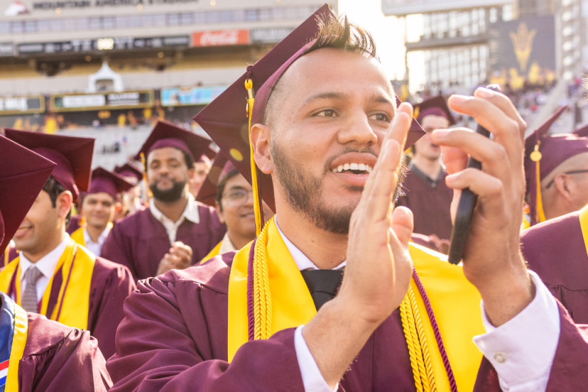 An ASU graduate claps while in the crowd at a commencement ceremony