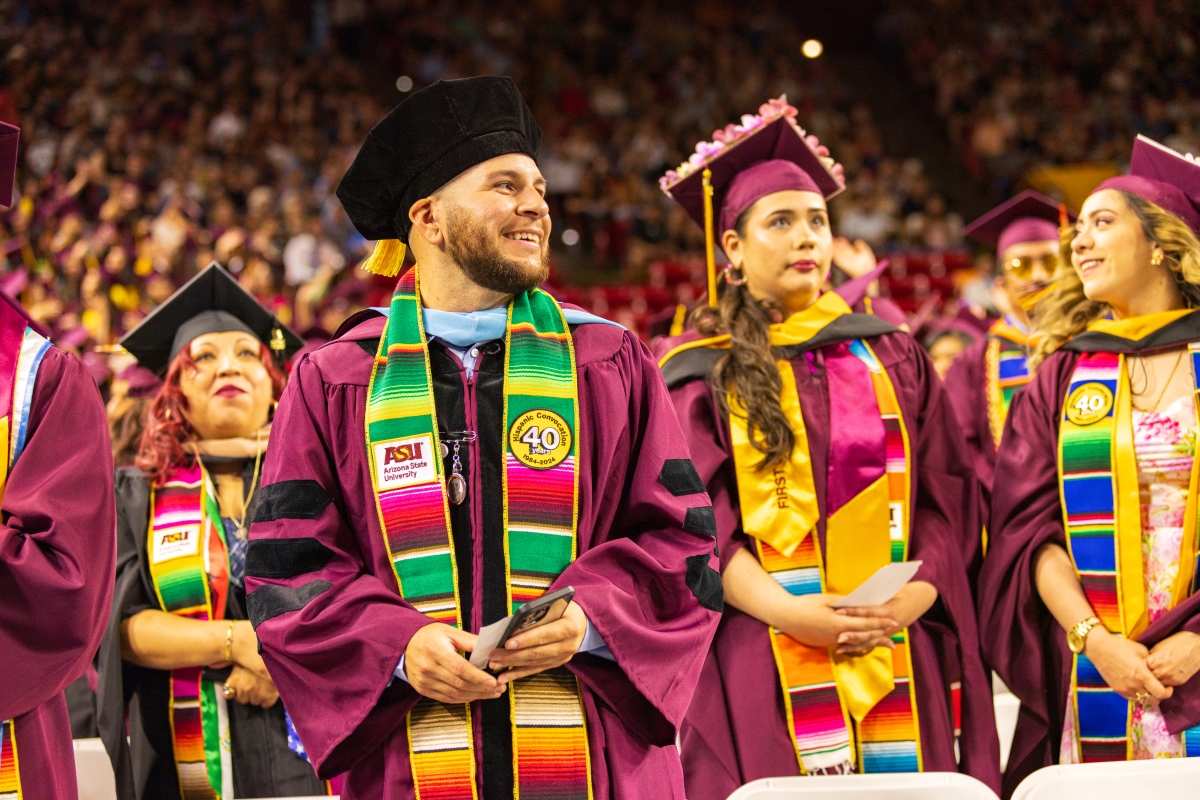 Students in maroon caps and gowns standing during Hispanic Convocation
