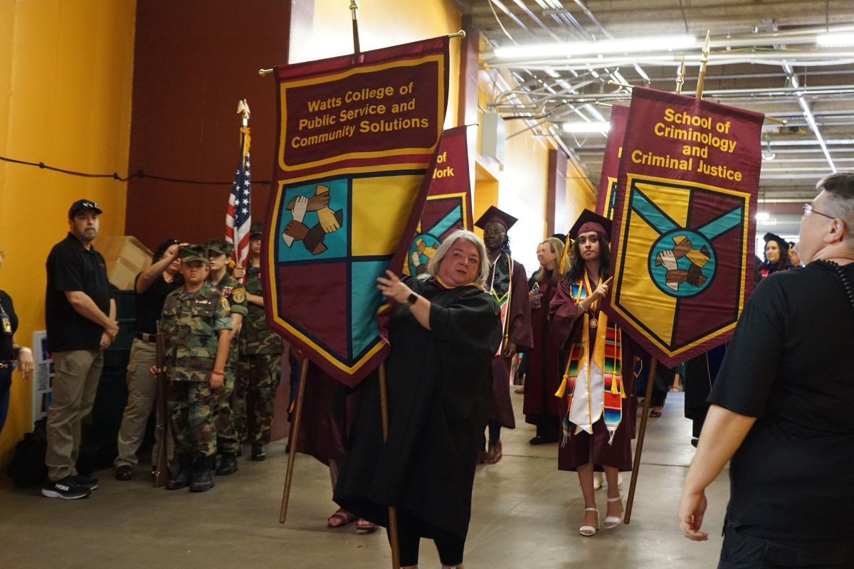 A crowded hallway filled with students in graduation regalia and others holding banners.