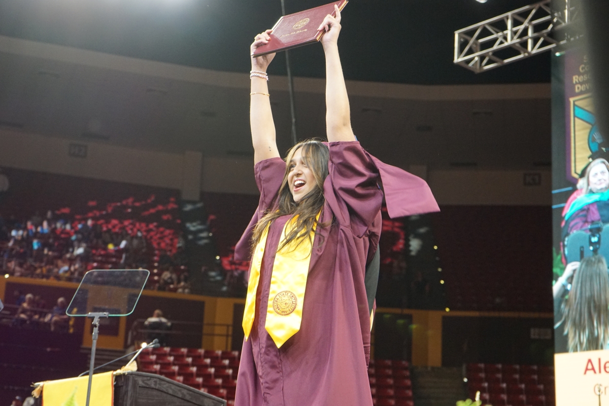 A graduate holds a diploma cover aloft