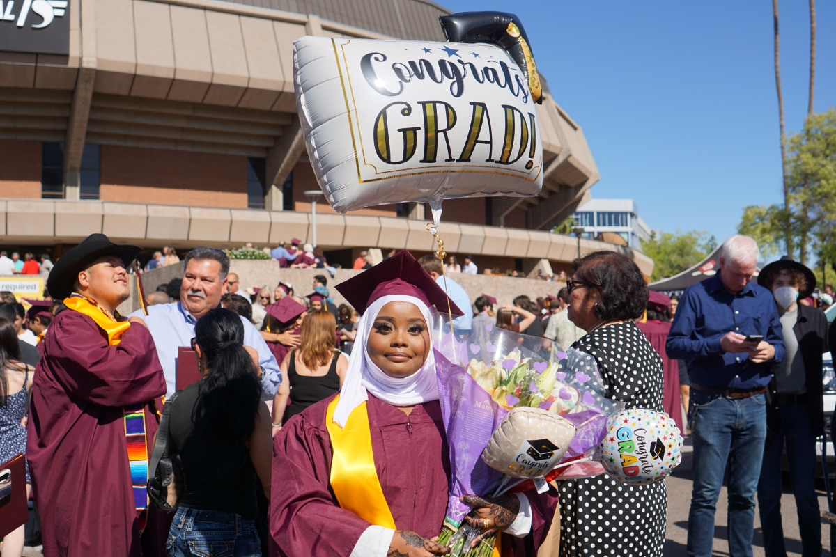 A graduate holds flowers with a balloon in the background that says 