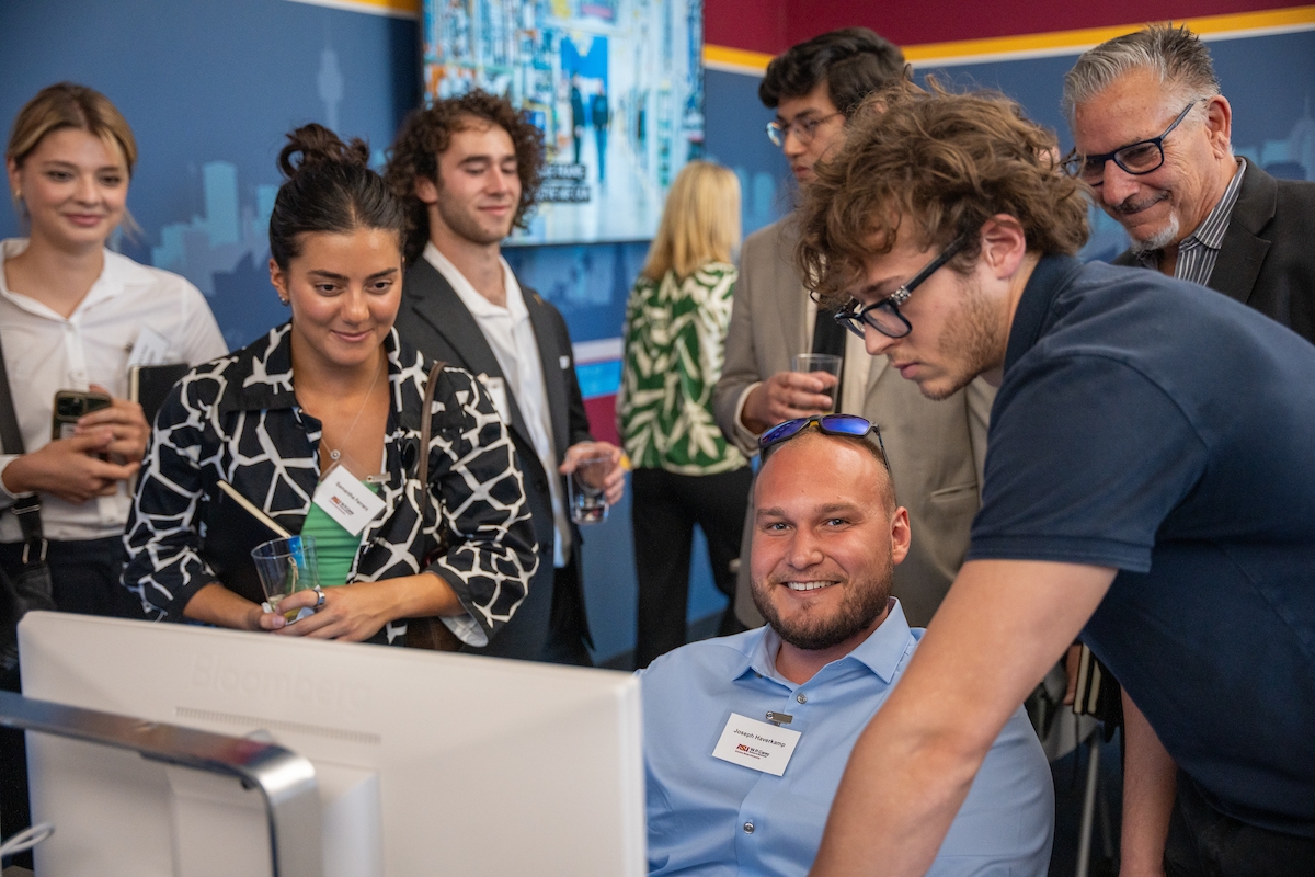 Students and guests gather around a computer smiling