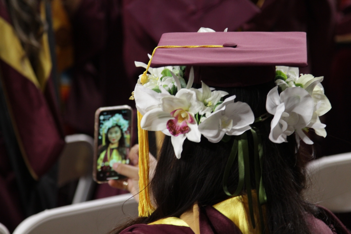 A graduate wearing a flower crown and graduation cap takes a selfie