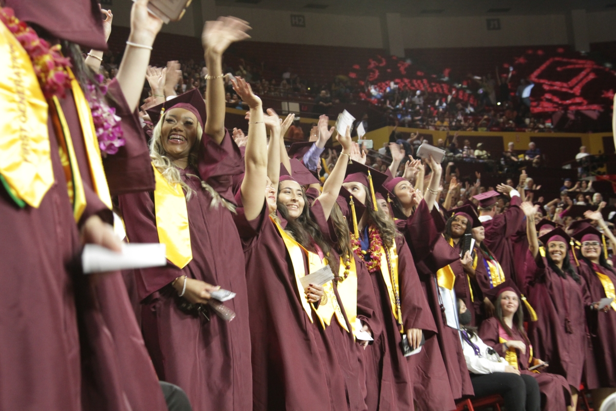 A line of graduates waving their arms in the air and smiling