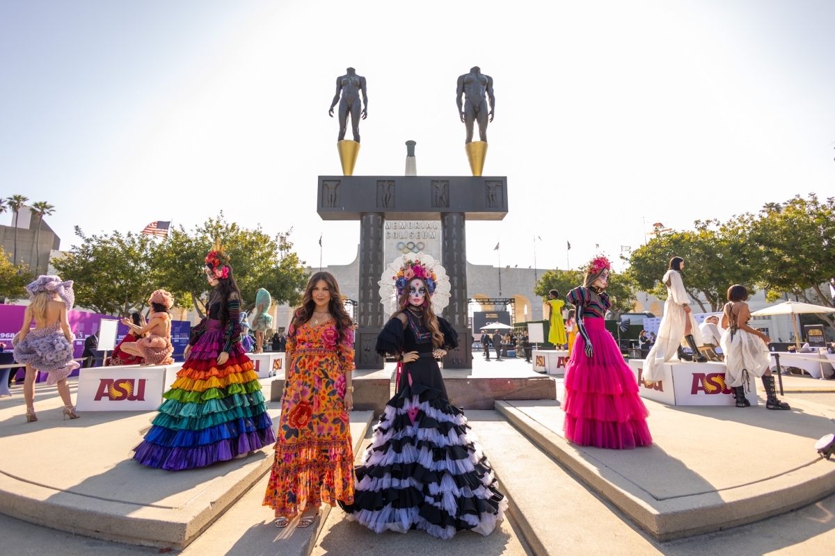 A woman in a long, colorful dress poses with models wearing long, colorful dresses, headdresses and face paint.