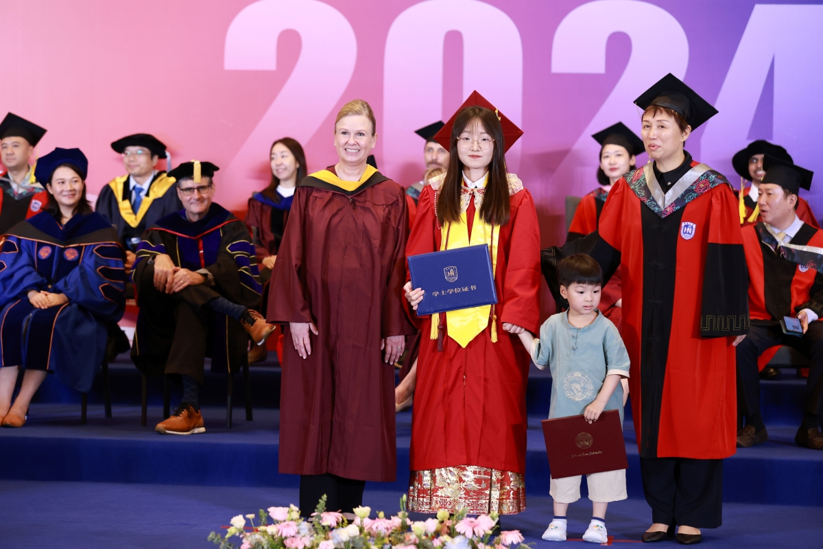 People wearing graduation regalia stand on stage with a small child.
