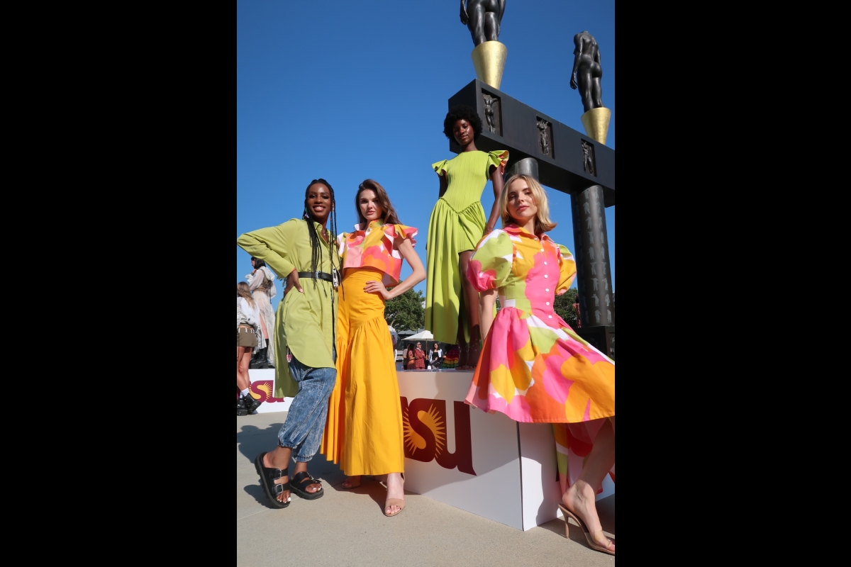 A group of models wearing colorful fashion designs poses with the designer.