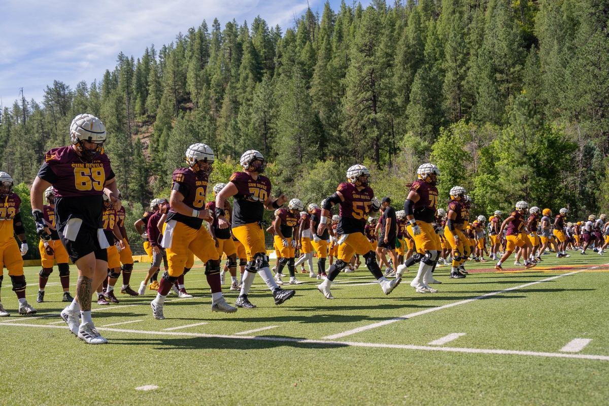 ASU football players practicing on a field surrounded by pine trees