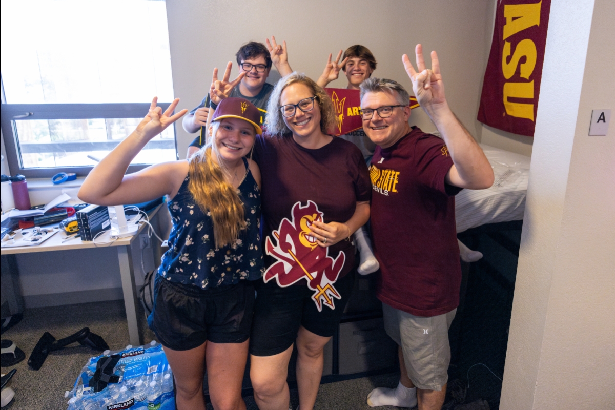 Family of five pose for photo making pitchfork sign with hands in dorm room