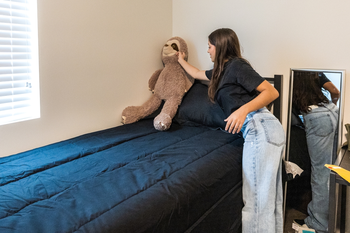 Young woman placing a stuffed animal on her dorm bed