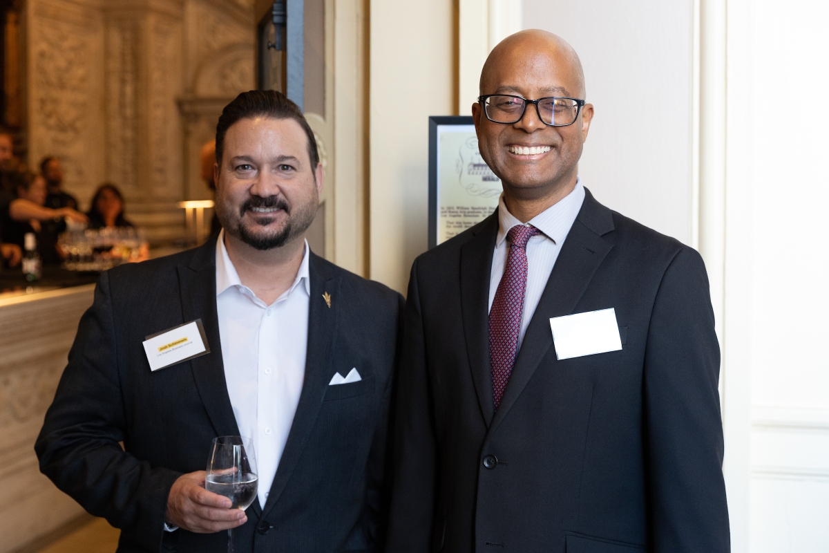 Two men in dark suit jackets pose for photo