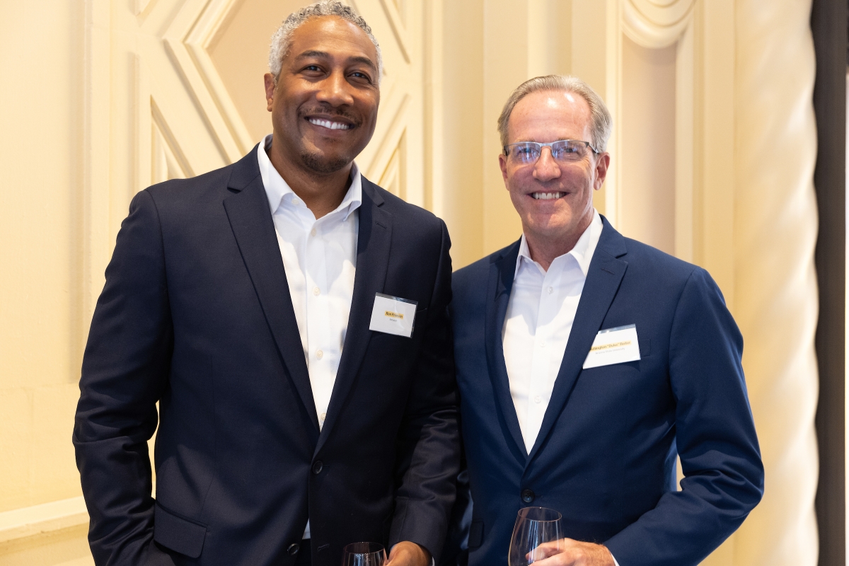 Two men in navy suits pose for a photo