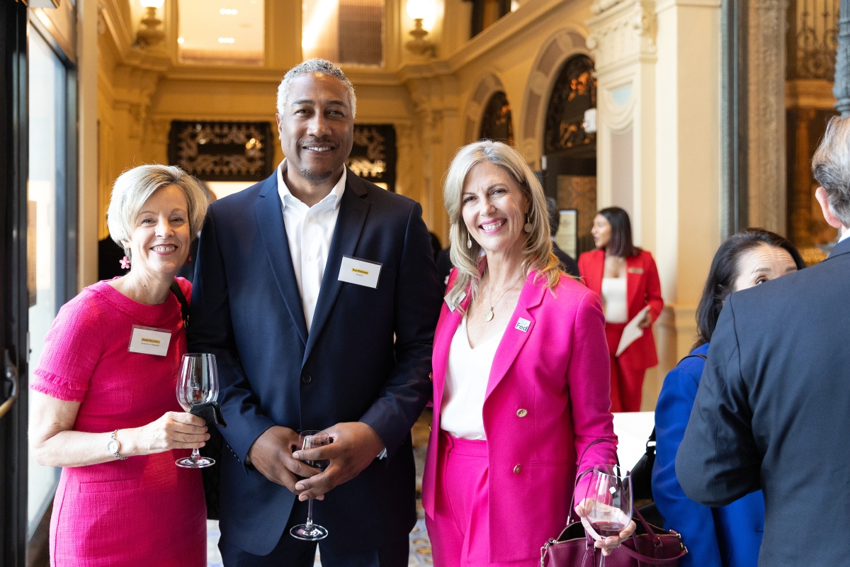 Two women in pink dresses and man in dark suit jacket pose for photo