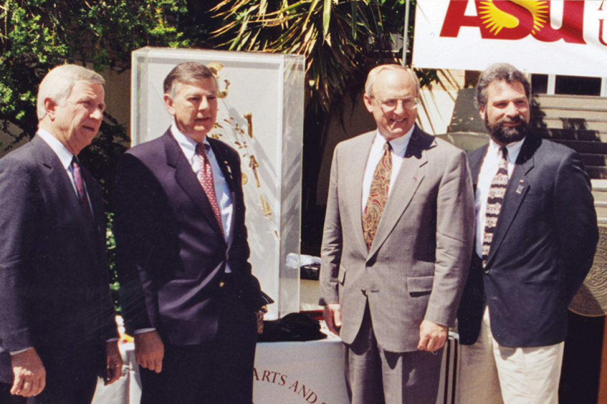 Four men in suits and ties pose for photo at a grand opening event