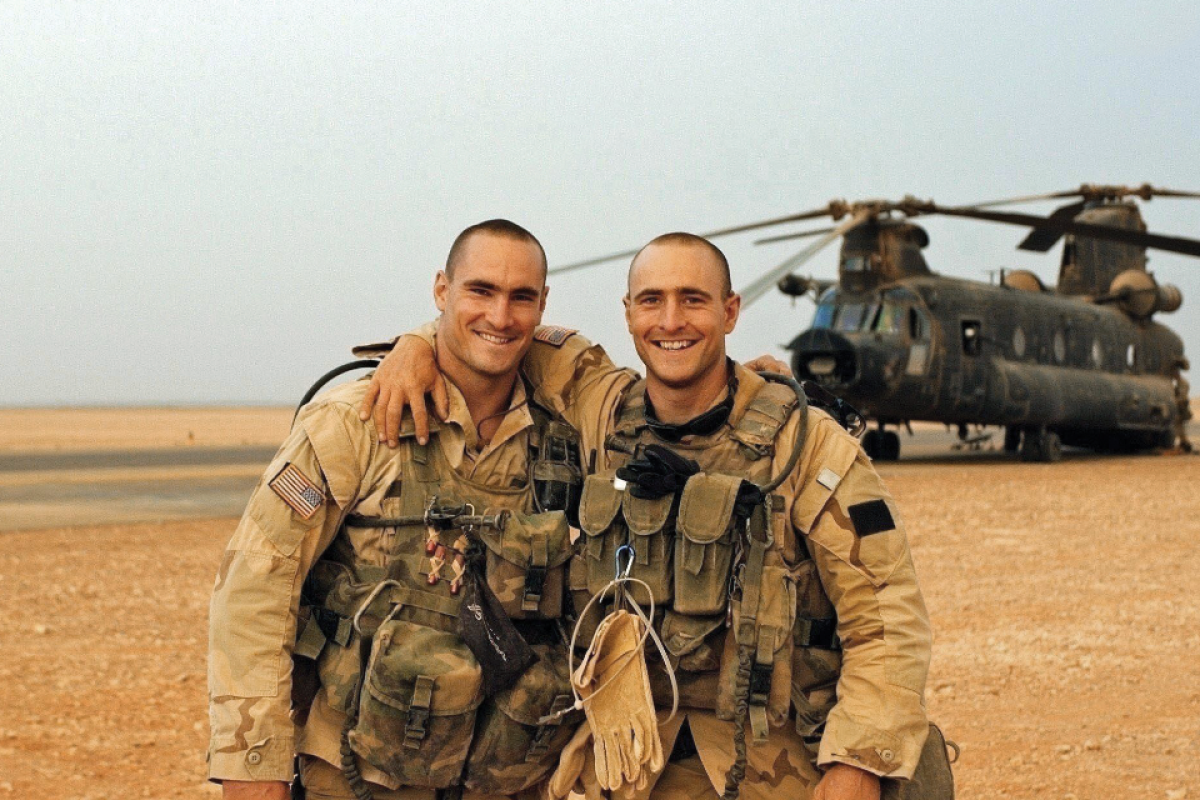 Two men wearing Army gear posing in front of helicopter in Afghanistan