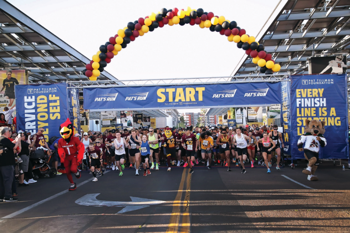 People at race start under large blue banners and maroon, gold and black balloons