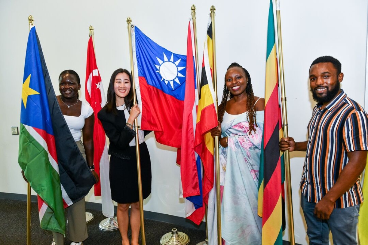 Four people holding flags representing different countries.