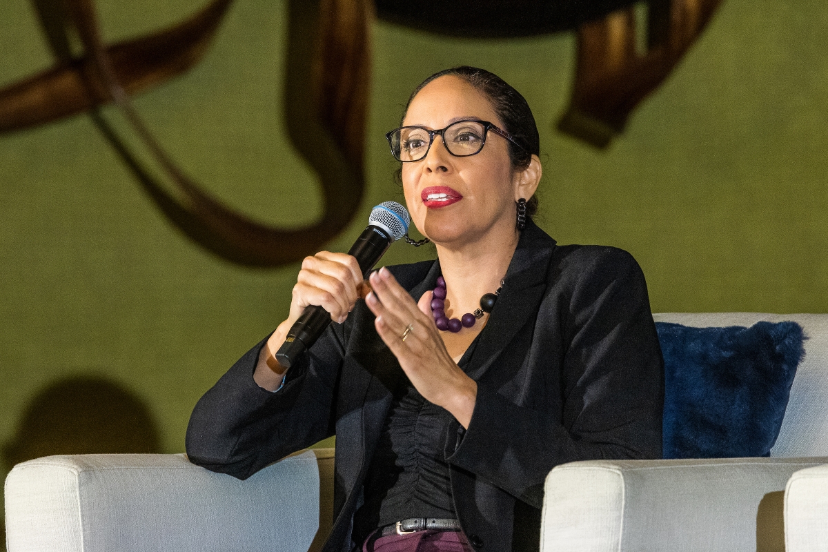 Woman seated on a stage speaking into a microphone.