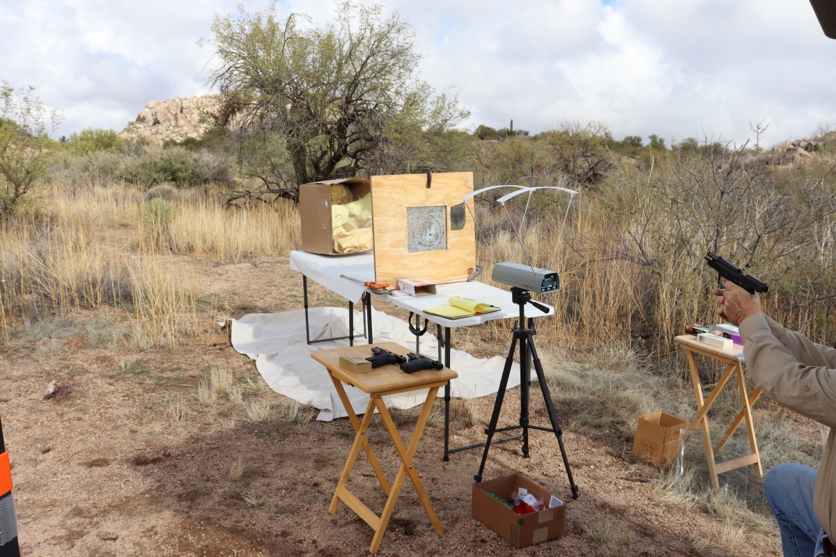 Equipment for a scientific experiment set up in the desert; arms hold a gun toward the setup on the right.