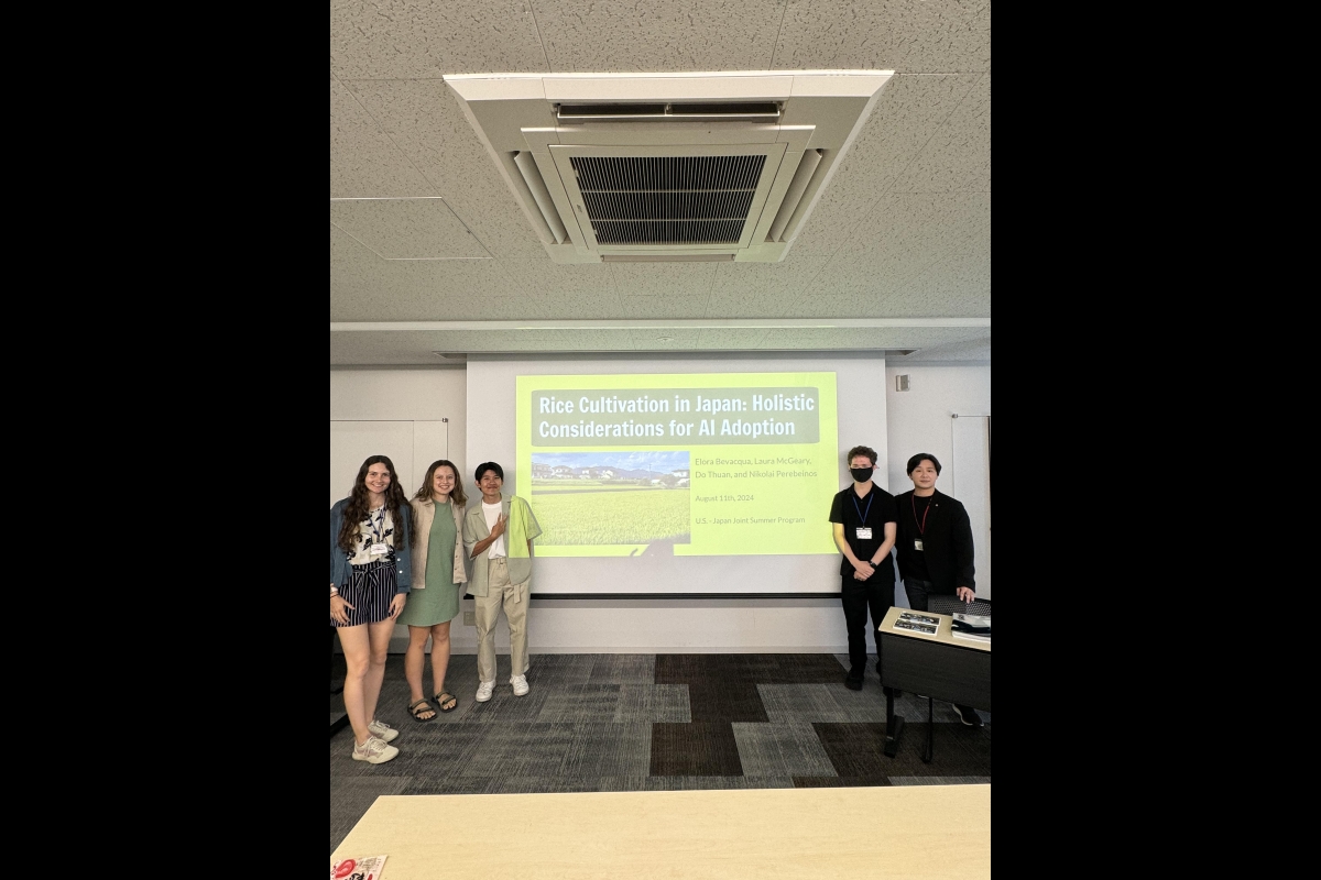 Five people stand around a presentation screen in a classroom.