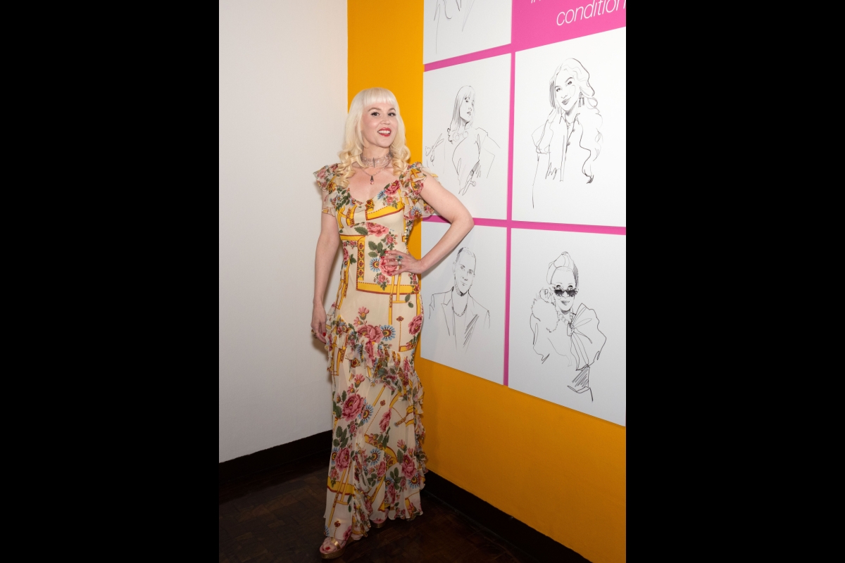 Woman in a floral dress stands in front of a wall of sketched portraits.