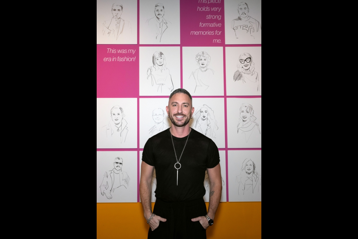 Man in a black shirt posing in front of a wall with sketched portraits on it.