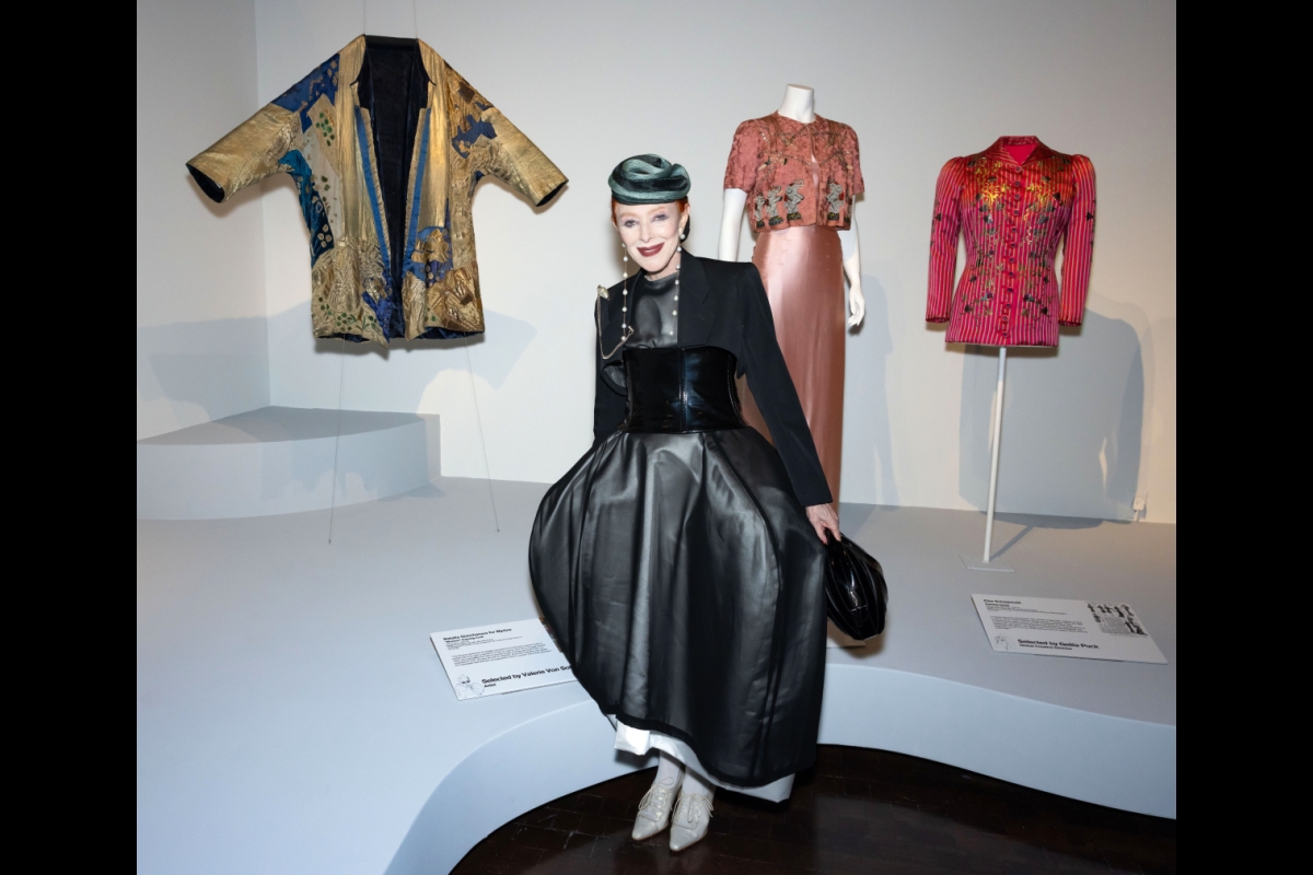 Woman in a black ensemble poses in front of manikins displaying various garments.