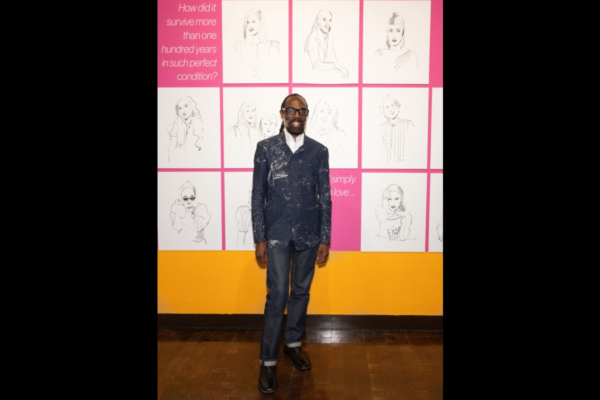 Man in a suit poses in front of a wall of sketched portraits.