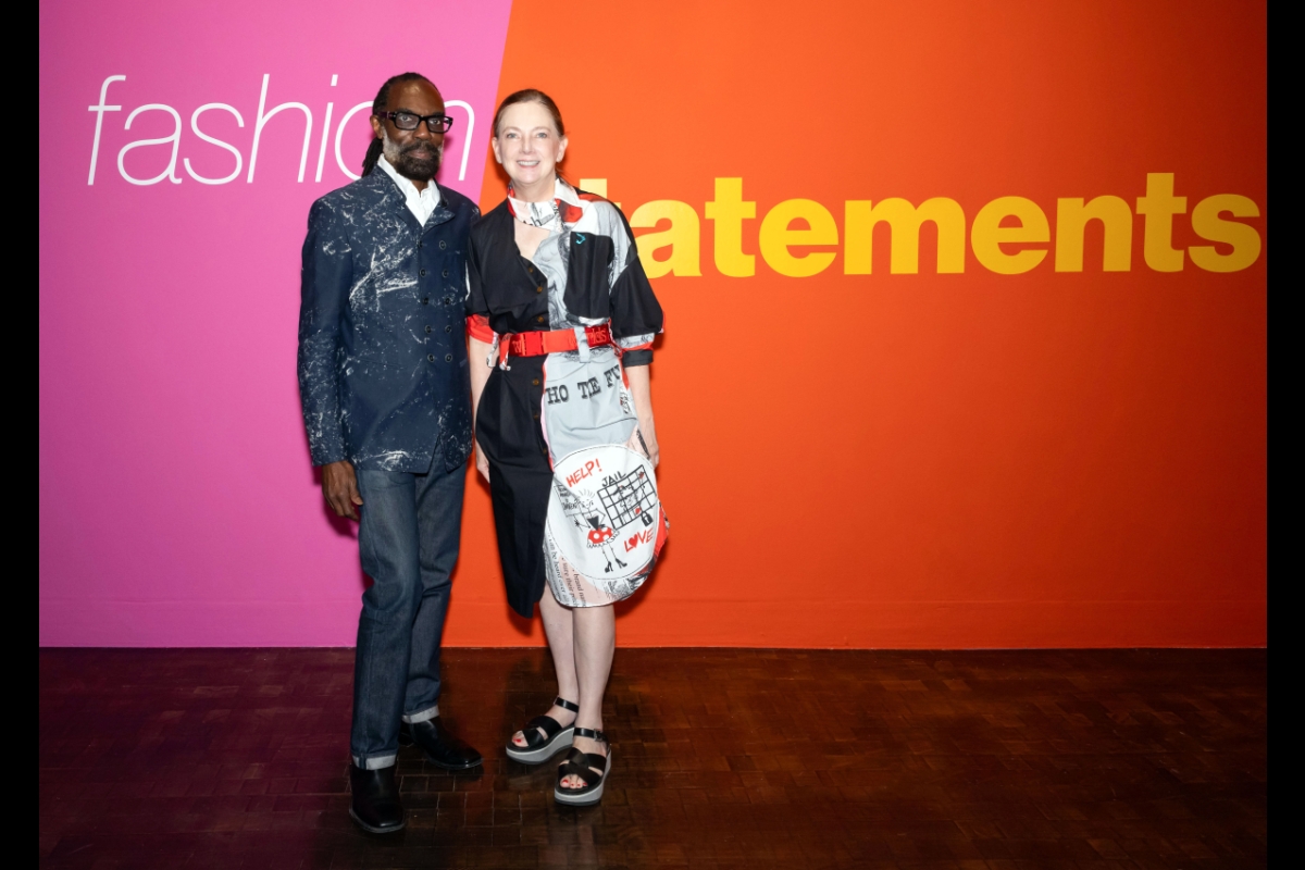 Two peole pose in front of a wall showing the words 