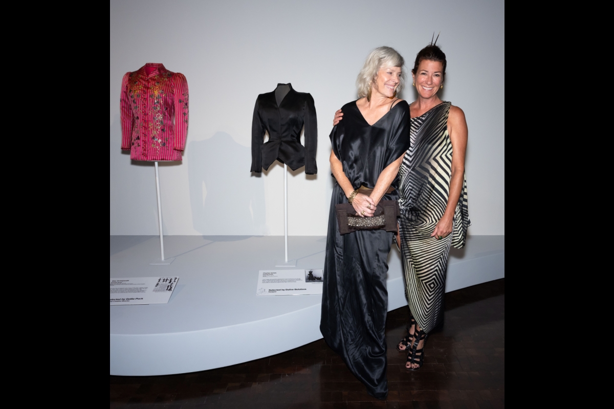 Two women pose next to garments on display in an exhibit.