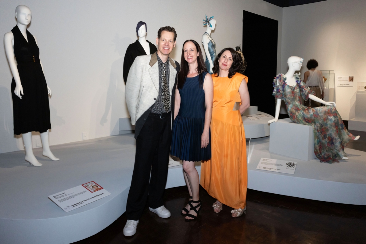 Three people pose next to garments on display in an exhibit.