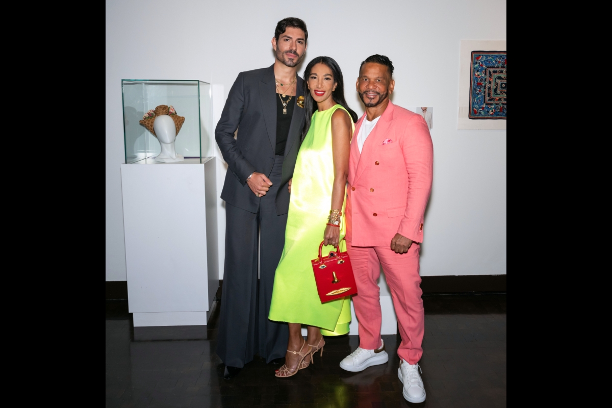 Three people pose next to a hat on display at an exhibit.