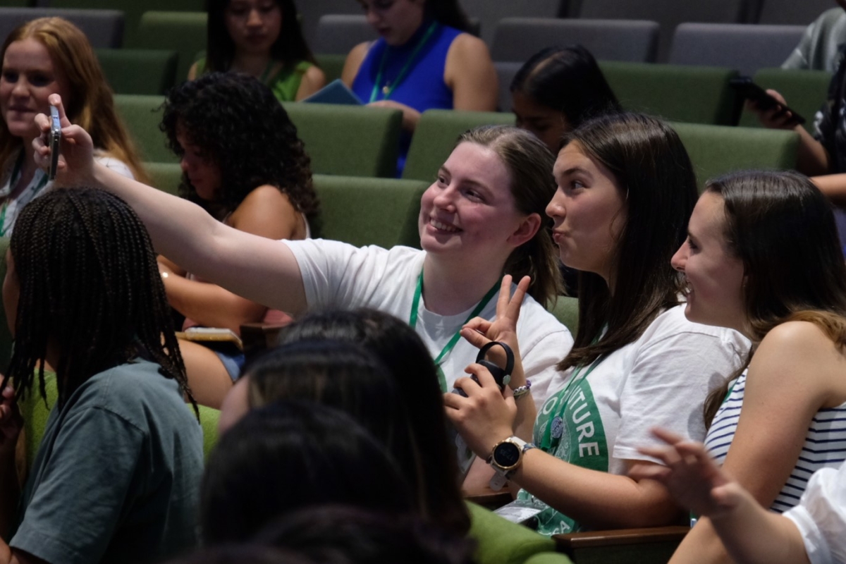 Youth delegates seated in an auditorium take a selfie.