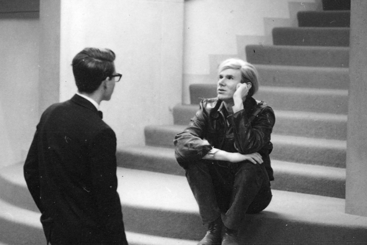 A man sits on steps and talks to another man