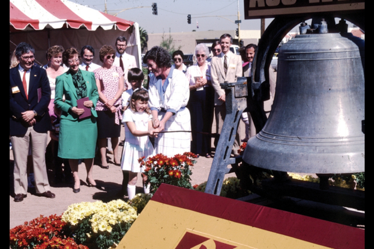 Historical photo of a crowd of people watching a mother and daughter ring a large bell