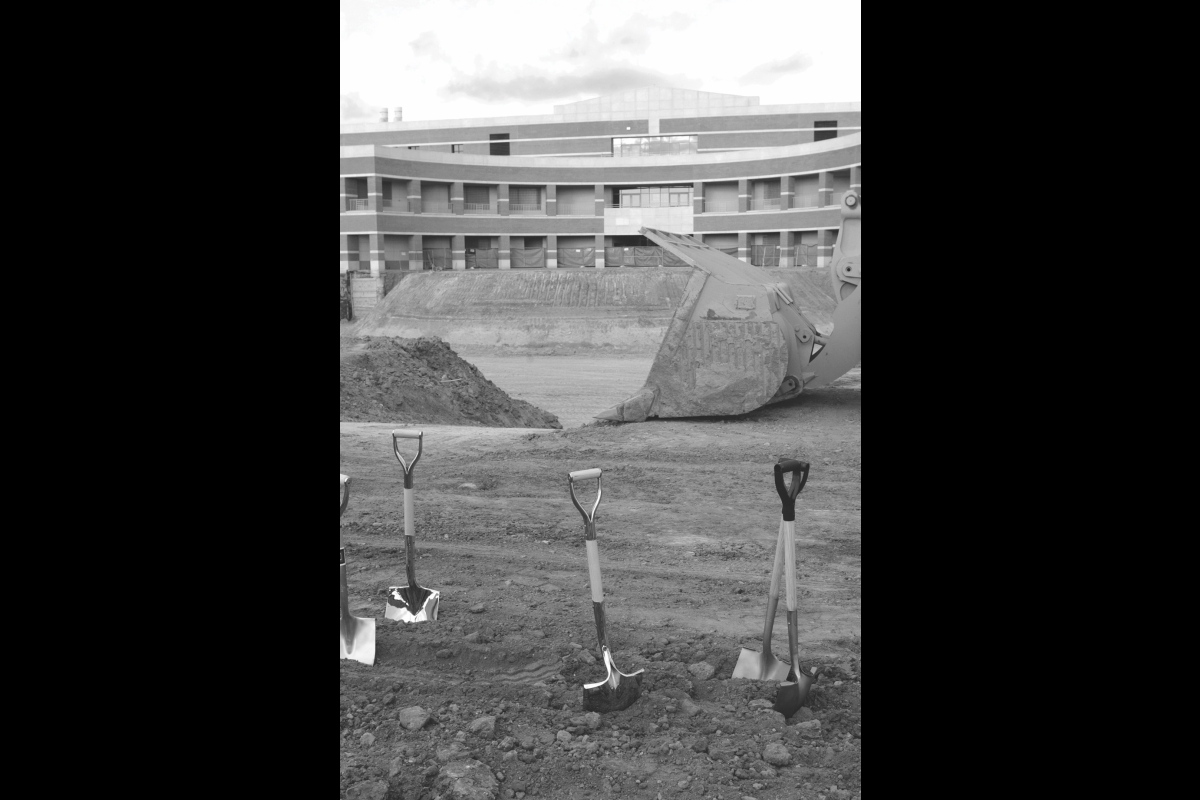 Black and white photo of shovels in dirt with a building under construction behind