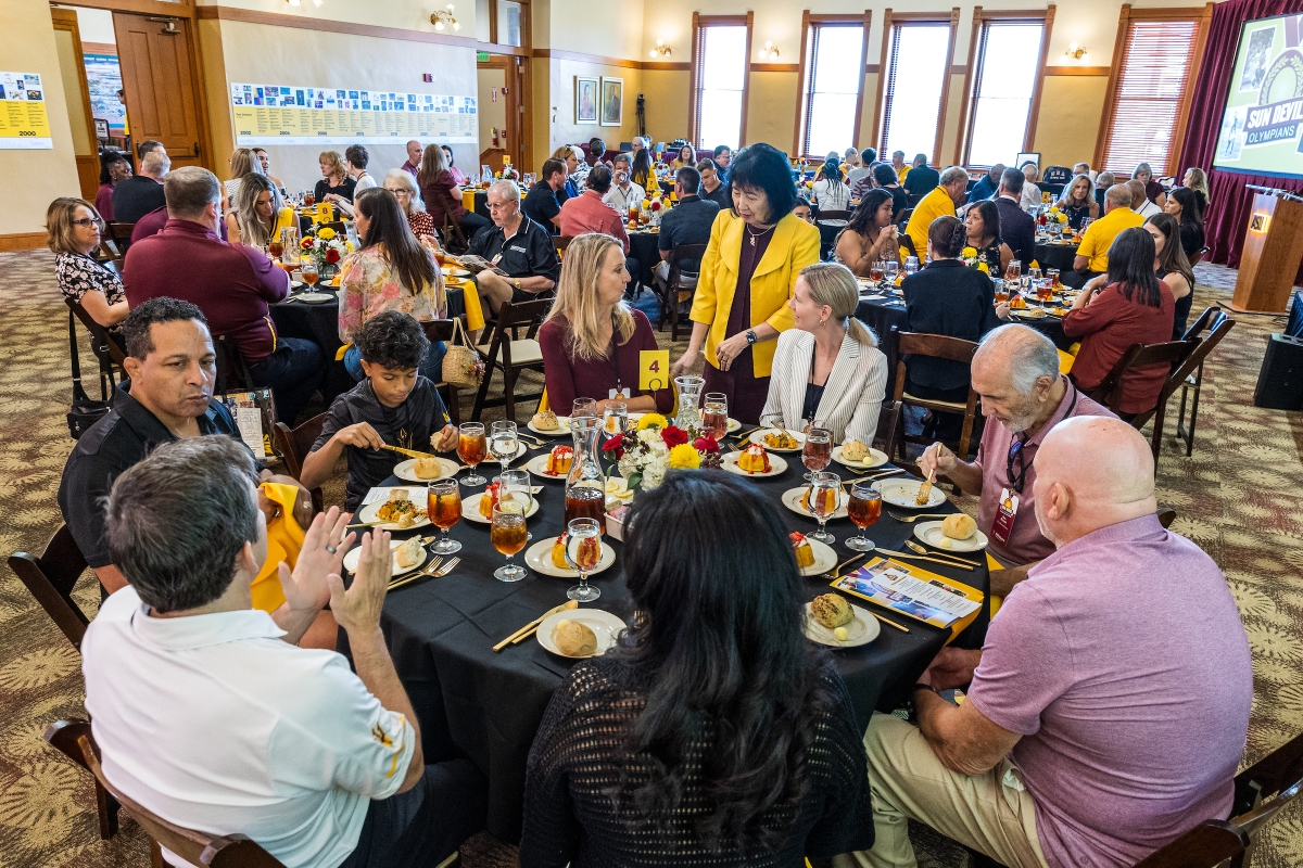 People seated at round tables eating a meal in a large ballroom.