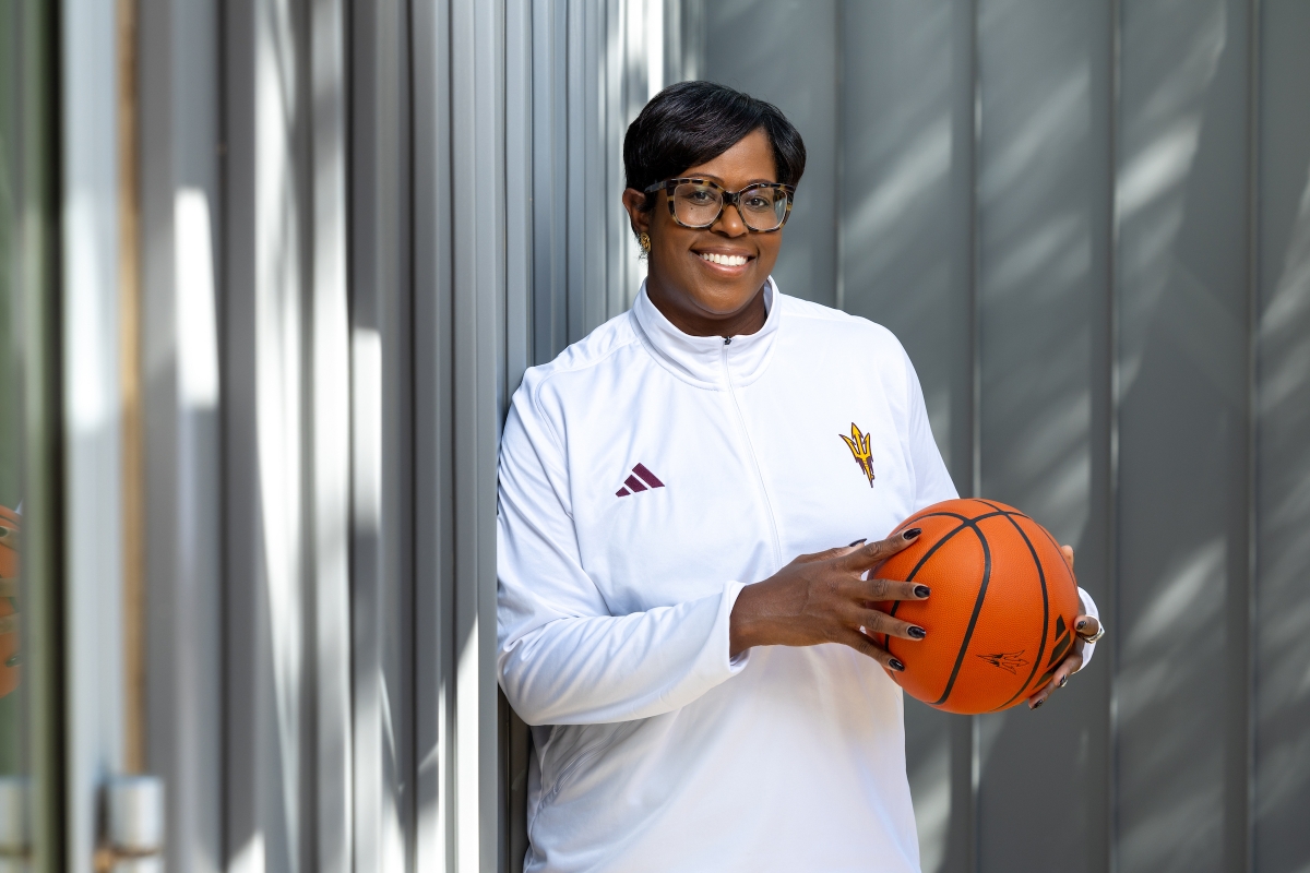 Portrait of a Black woman wearing a white track suit jacket and glasses holding a basketball