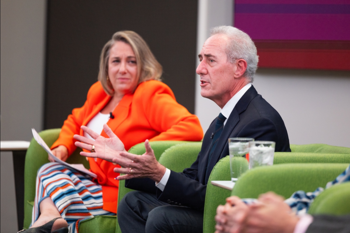 A woman and a man sit in front of a large room full of people