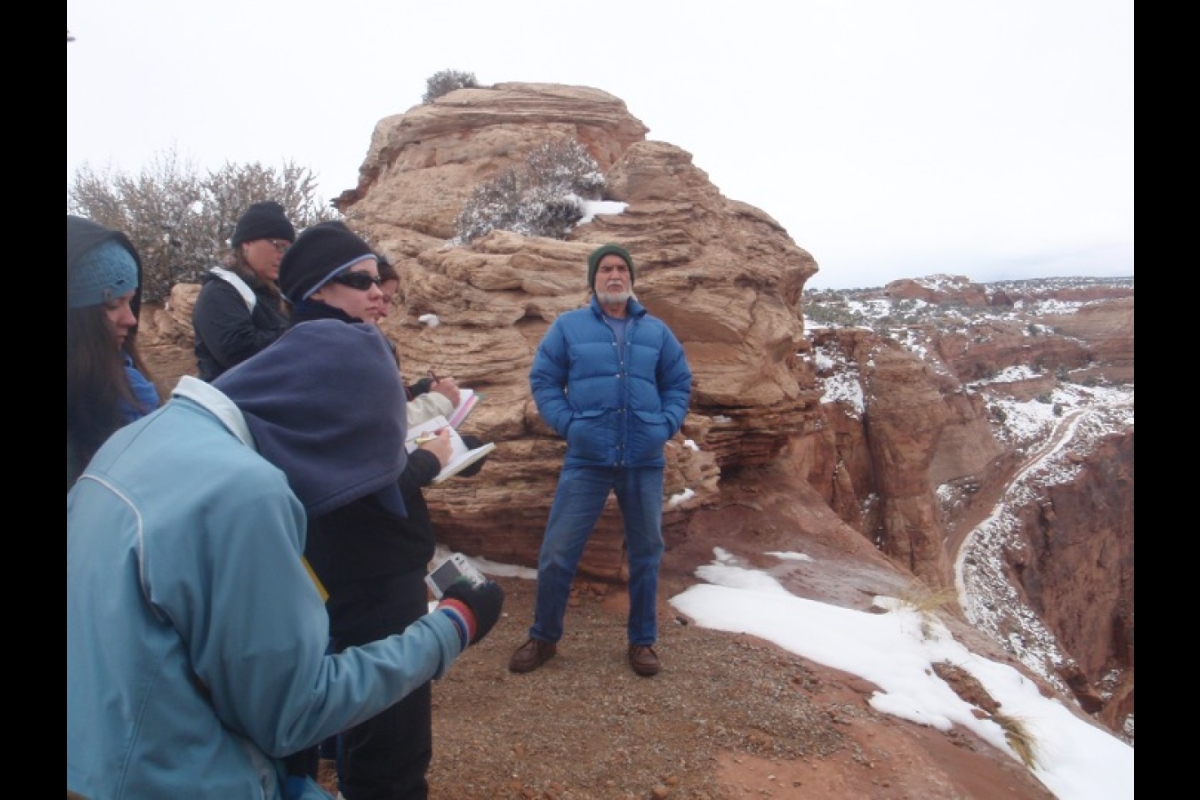 Man standing at the base of a large rock as students take notes.