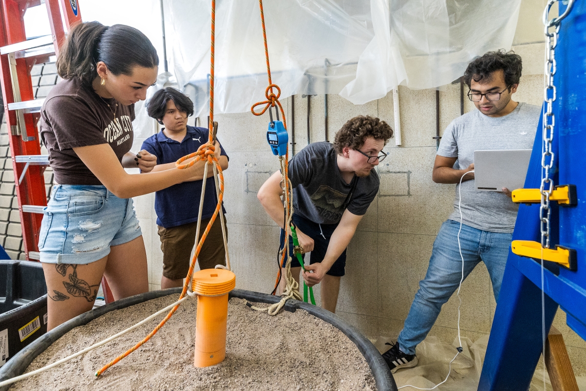 Students work together on testing an anchor in a large barrel of sand in a lab