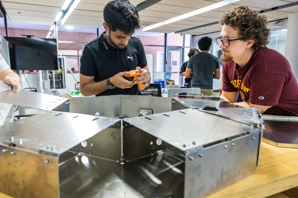 Two students work on a metal construction piece in an ASU lab