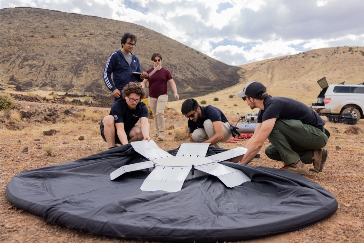 Students test black circular inflatable landing pad at a crater site in Flagstaff